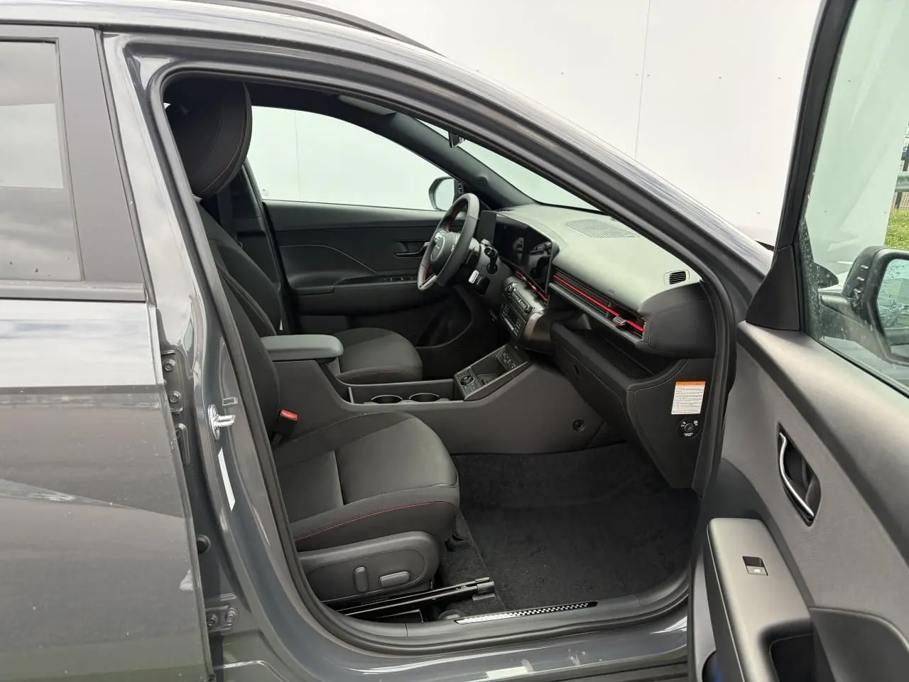 Intérieur côté conducteur du Hyundai Kona 2026 gris Ecotronic, avec sièges noirs et détails rouges sur tableau de bord.