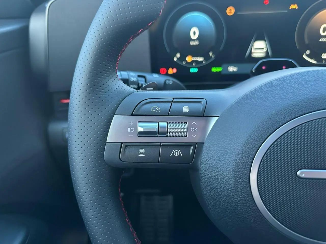 Gros plan sur le volant cuir perforé avec commandes multifonctions du Hyundai Kona II gris Ecotronic, tableau de bord numérique en arrière-plan.