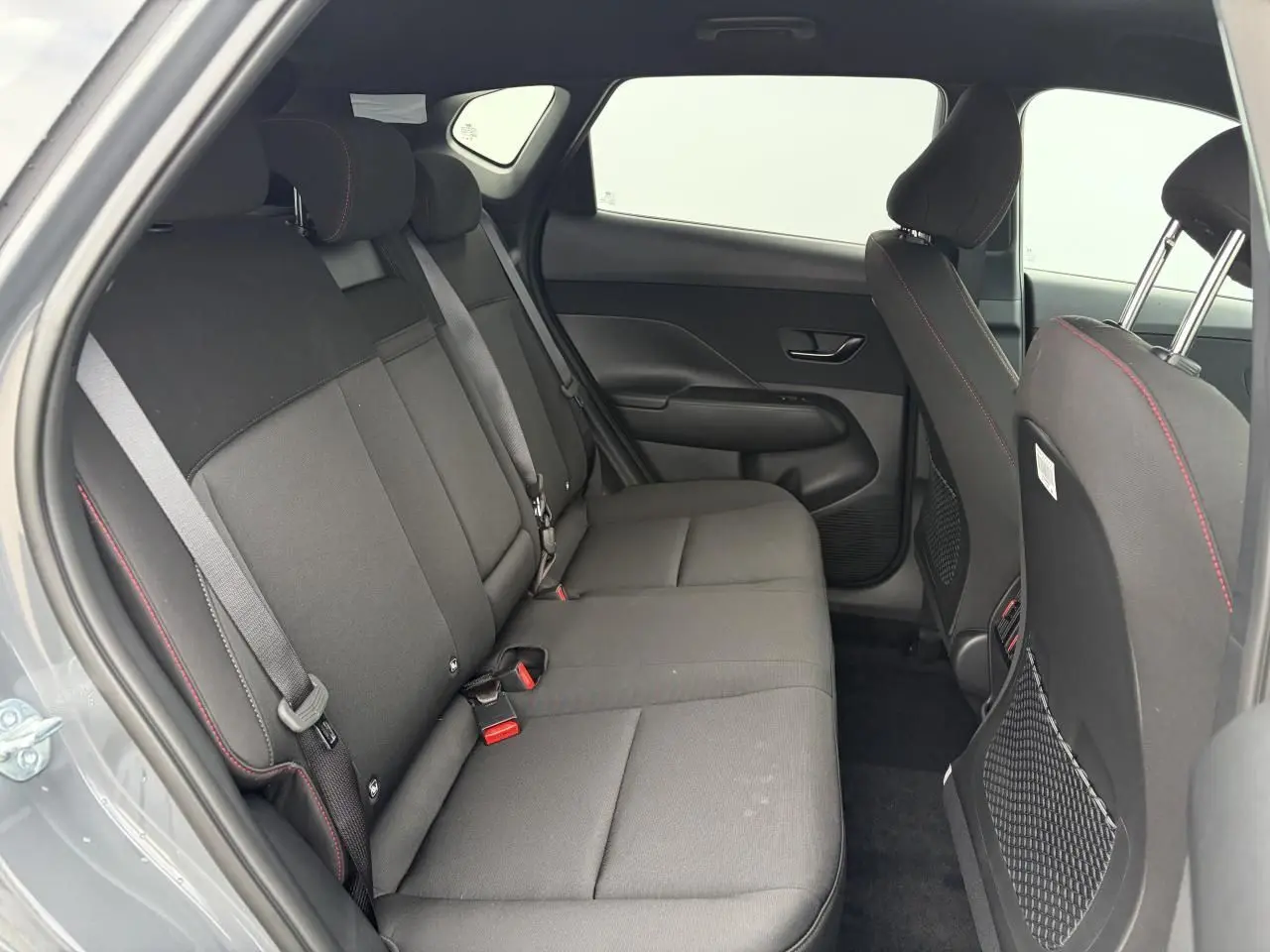 Vue intérieure côté gauche sur la banquette arrière noire avec surpiqûres rouges du Hyundai Kona 2026 gris métallisé.