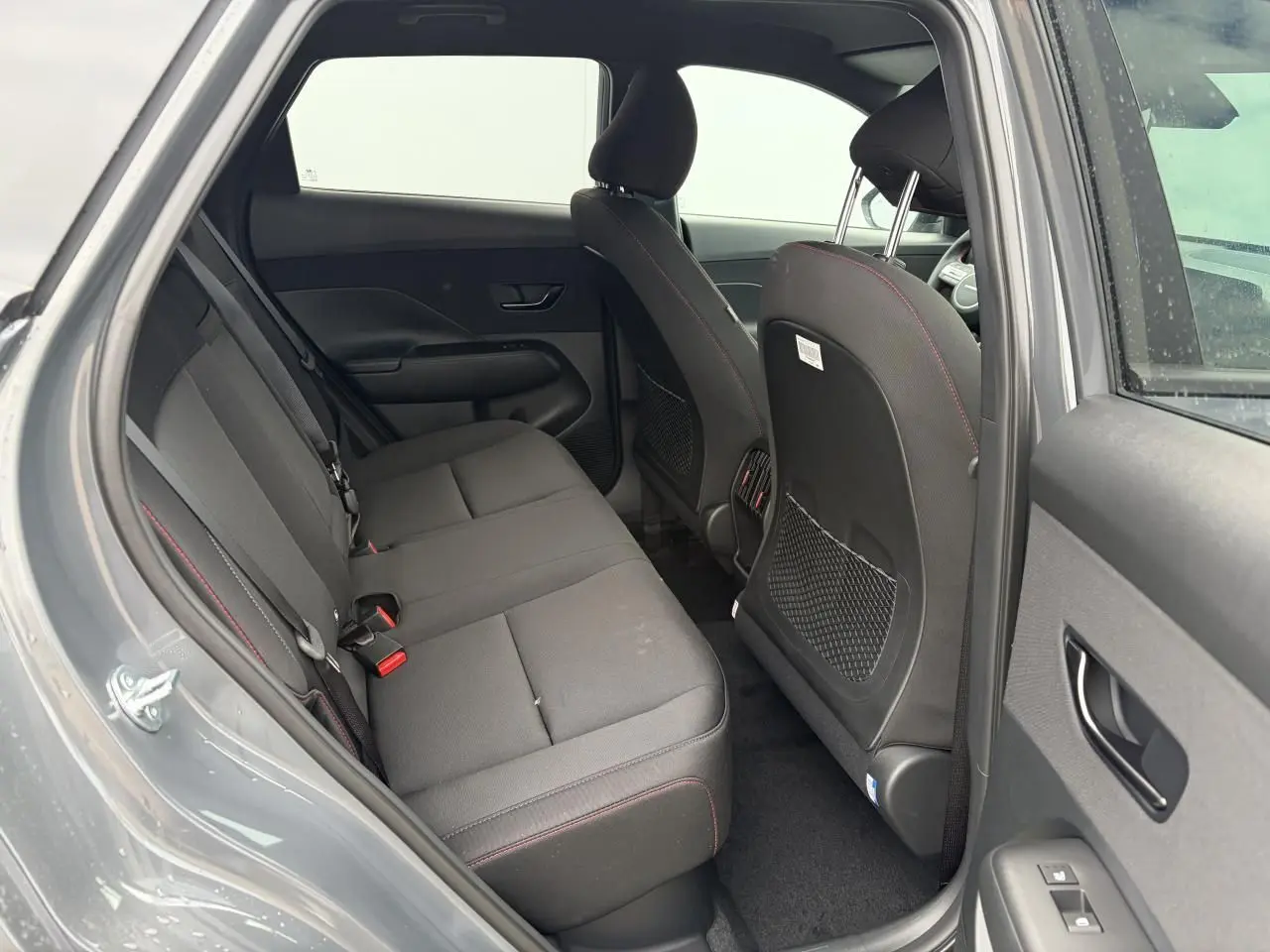 Vue intérieure arrière côté gauche du Hyundai KONA 2026 gris Ecotronic avec sièges tissu noir et surpiqûres rouges.