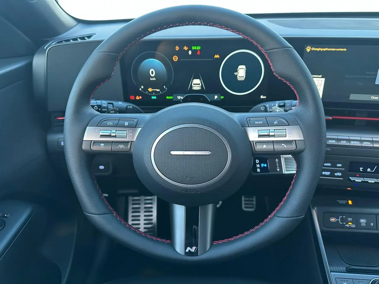 Vue rapprochée du volant cuir noir avec surpiqûres rouges du Hyundai Kona 2026, tableau de bord numérique et commandes intégrées.