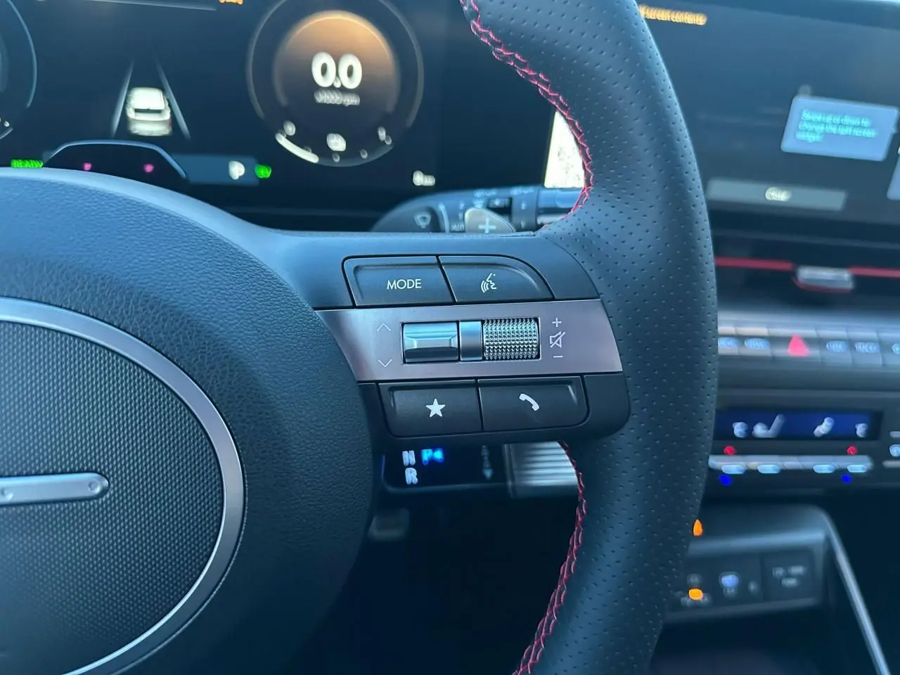 Gros plan sur le volant cuir perforé avec surpiqûres rouges du Hyundai Kona 2026, affichage numérique en arrière-plan.