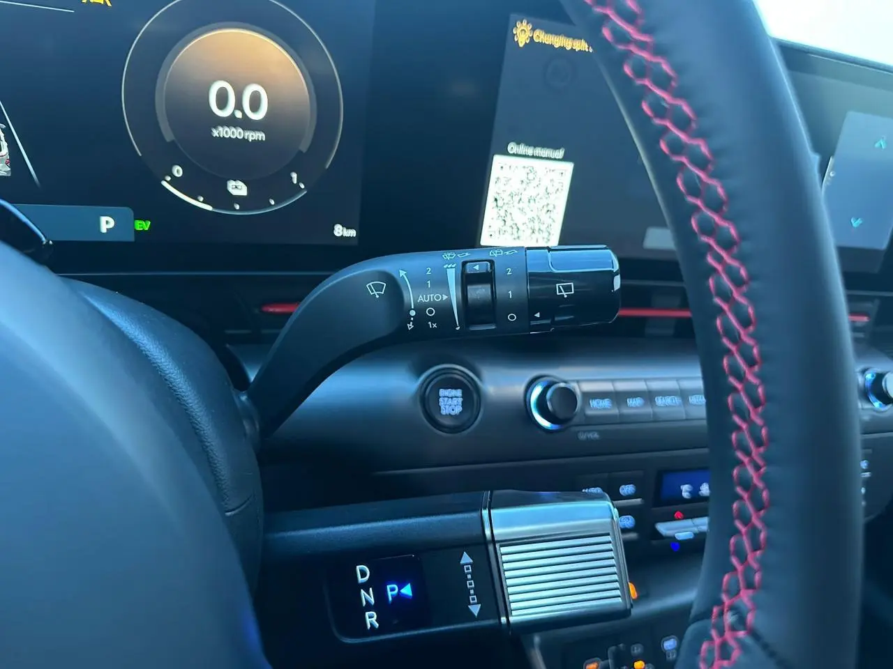 Gros plan intérieur sur le volant cuir noir avec surpiqûres rouges et levier de vitesses du Hyundai Kona II gris Ecotronic.