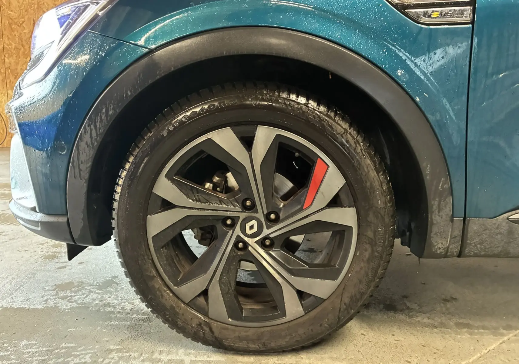 Gros plan sur la roue avant gauche du Renault Arkana bleu 1.3 TCE 140 RS-LINE avec jante noire et détail rouge.