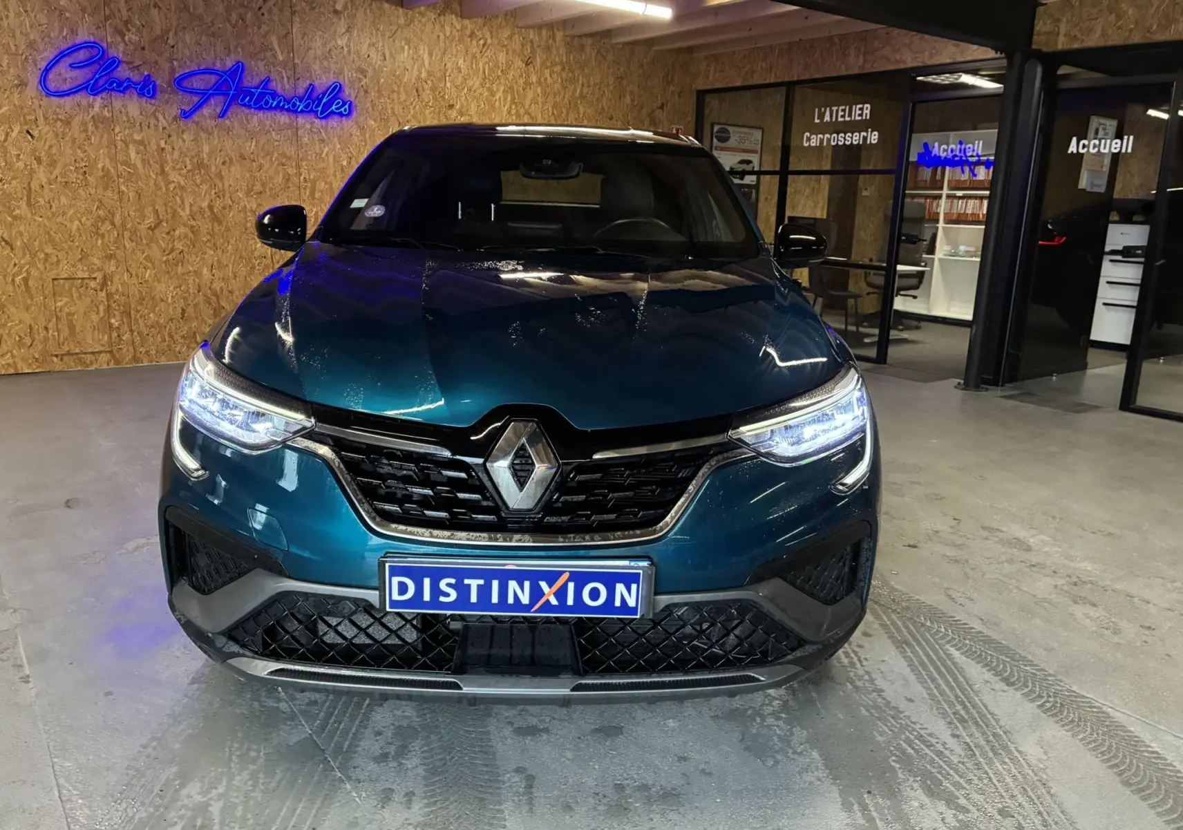 Vue frontale d'un Renault Arkana bleu 1.3 TCE 140 RS-LINE avec phares allumés dans un showroom intérieur.