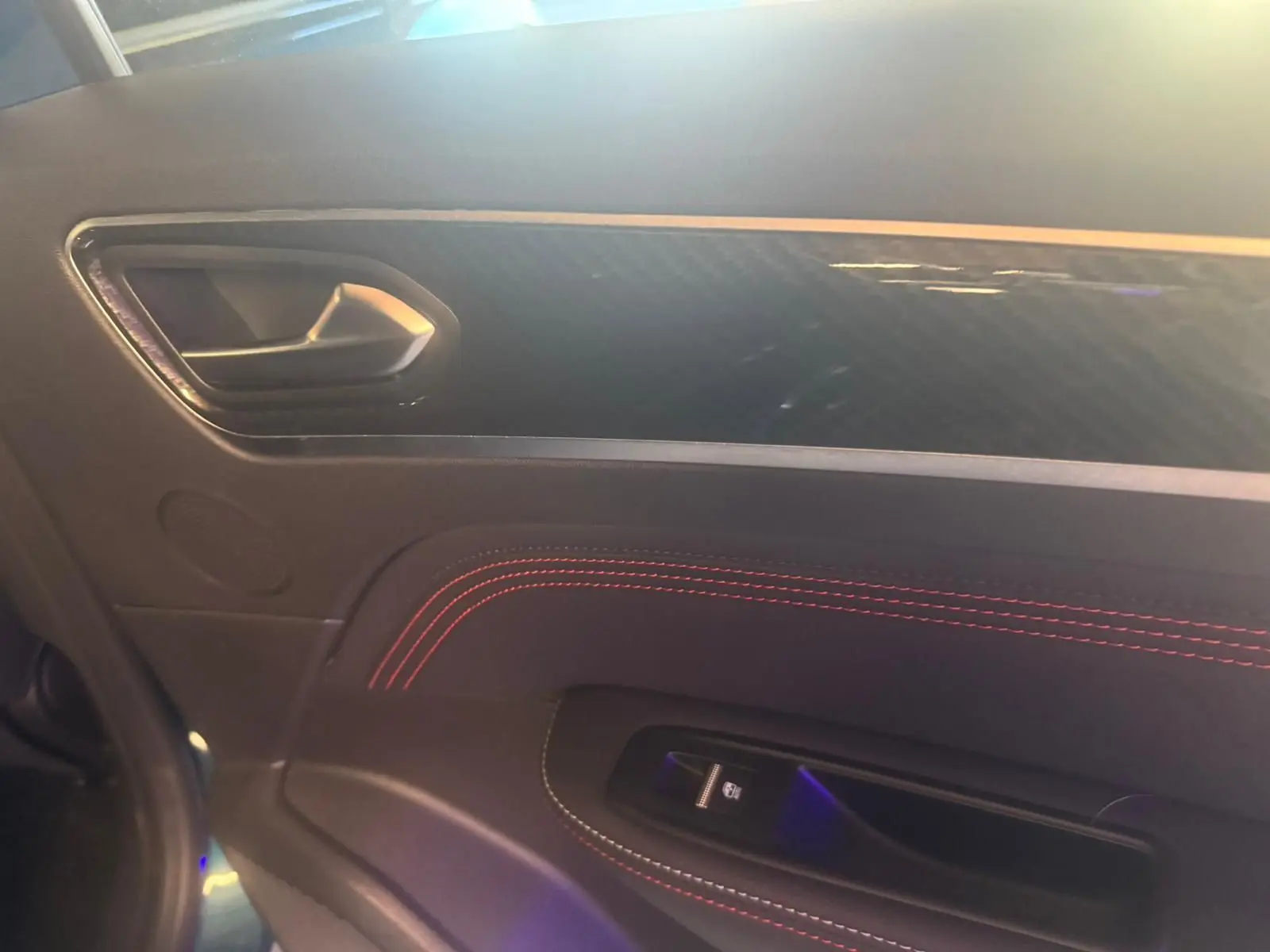 Détail de la porte intérieure côté gauche du Renault Arkana bleu, avec surpiqûres rouges et poignée argentée.