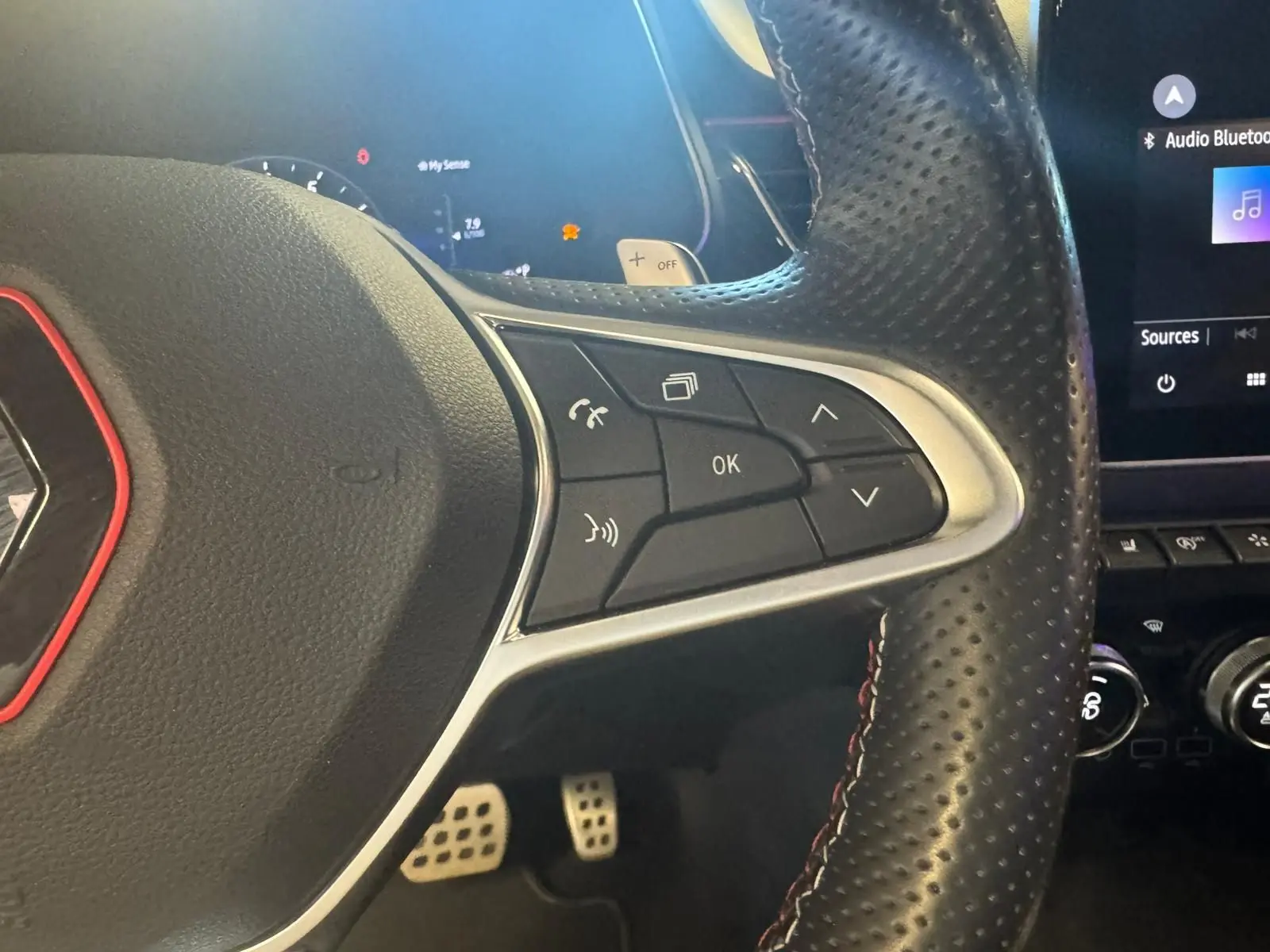 Gros plan sur le volant en cuir noir perforé du Renault Arkana 1.3 TCE 140 RS-LINE avec commandes intégrées et surpiqûres rouges.