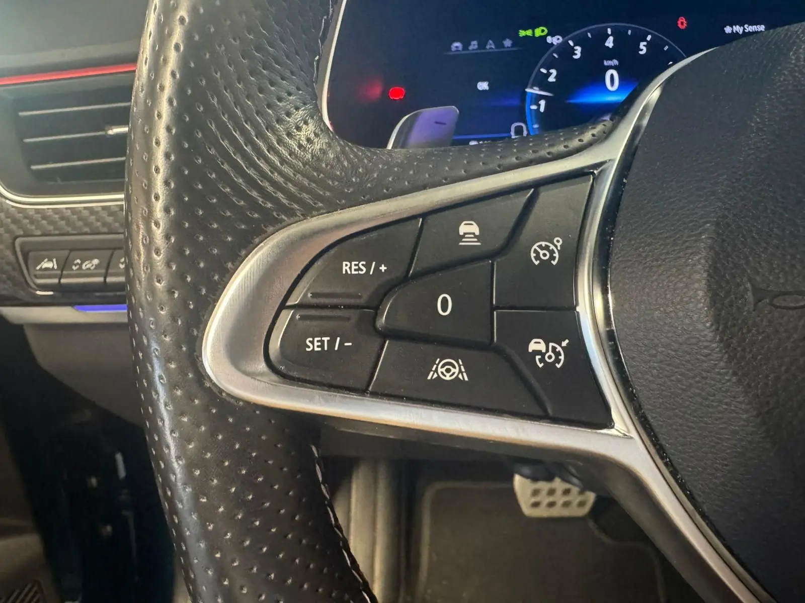 Gros plan sur les commandes au volant côté gauche du Renault Arkana bleu 1.3 TCE 140 RS-LINE avec affichage numérique en arrière-plan.