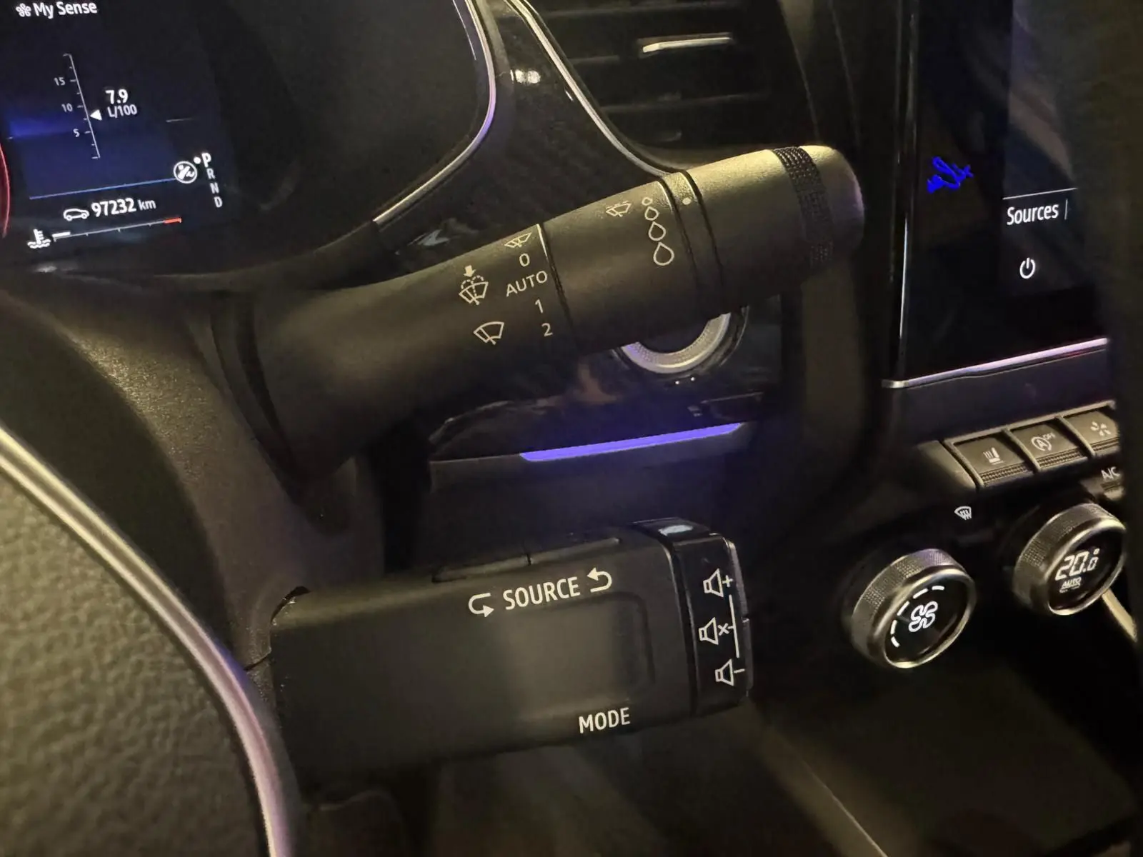 Gros plan sur les commandes de volant et tableau de bord noir du Renault Arkana bleu, avec affichage digital et régulateur de climatisation.