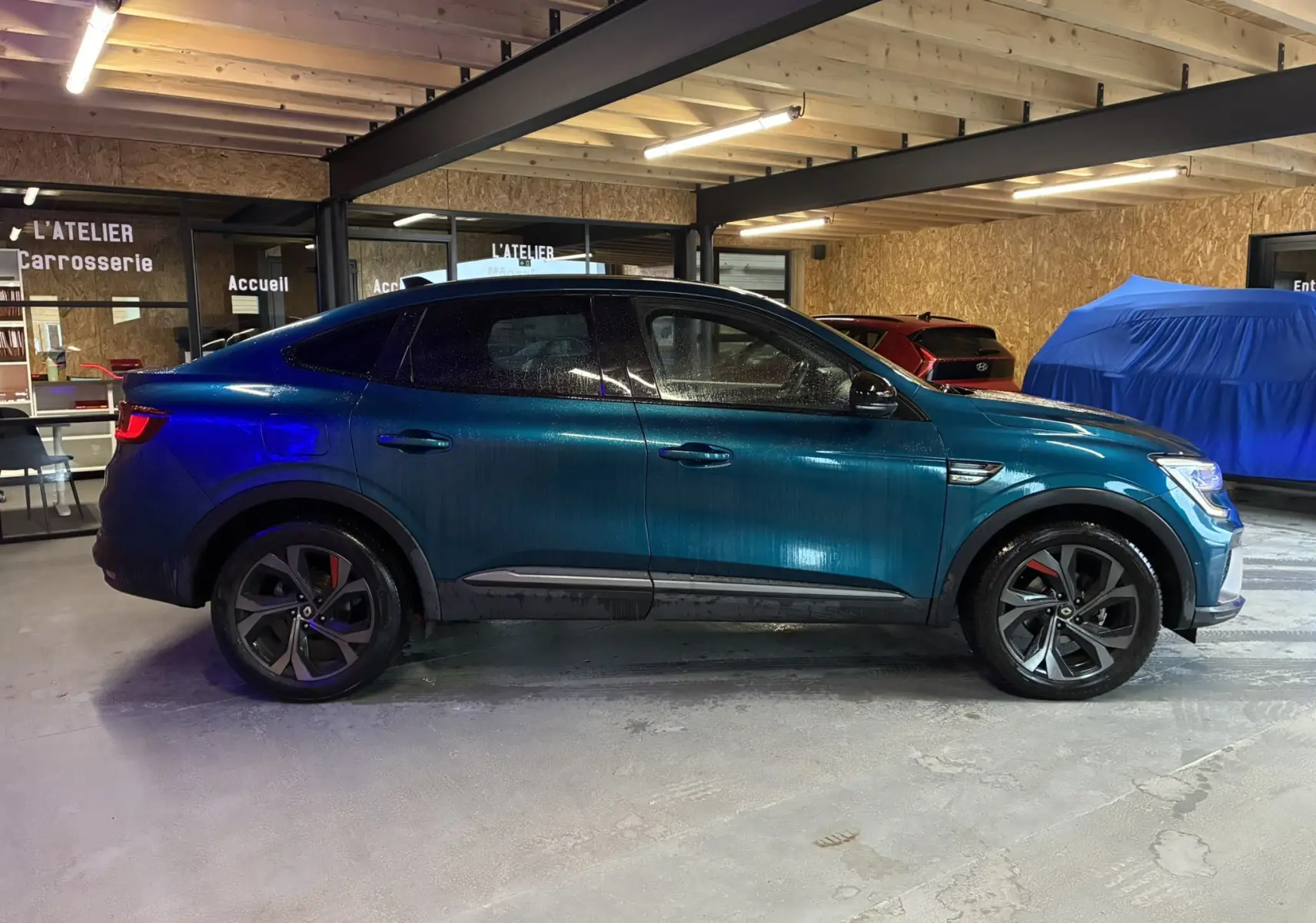 Vue de profil côté gauche d'un Renault Arkana bleu 1.3 TCE 140 RS-LINE en intérieur avec jantes noires et étriers rouges.