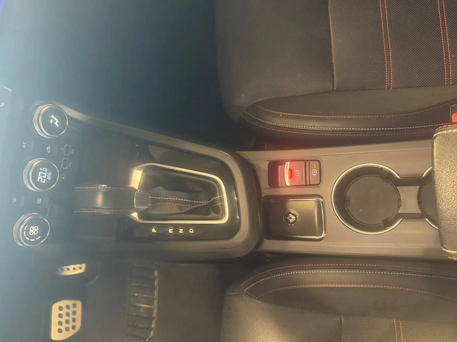 Vue plongeante sur la console centrale noire du Renault Arkana bleu, avec levier de vitesse automatique et sièges à surpiqûres rouges.