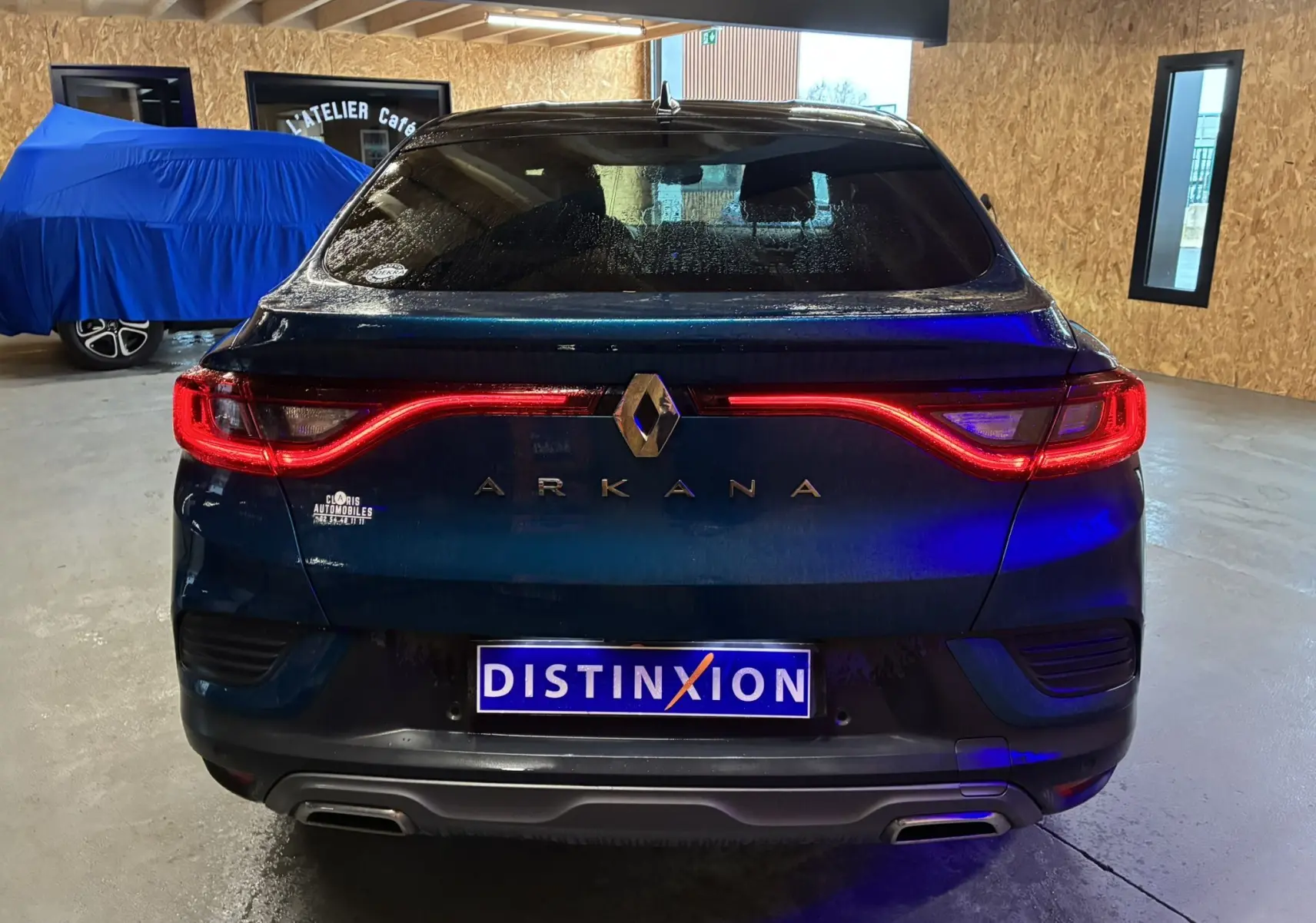 Vue arrière du Renault Arkana bleu 2021 avec feux LED allumés et double sortie d'échappement en intérieur d'atelier.