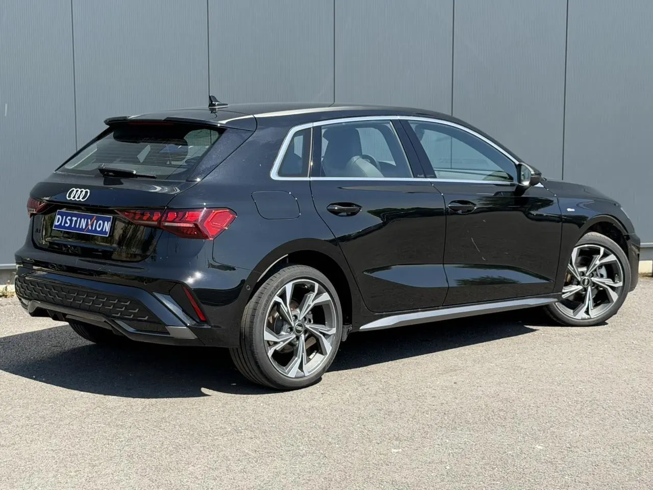 Audi A3 Sportback noir Mythe vue 3/4 arrière droit, avec jantes alliage 5 branches en Y et détails S-Line visibles.