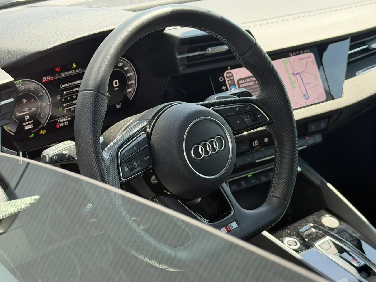 Vue rapprochée du volant sport en cuir perforé avec logo Audi S, tableau de bord numérique et écran central tactile.