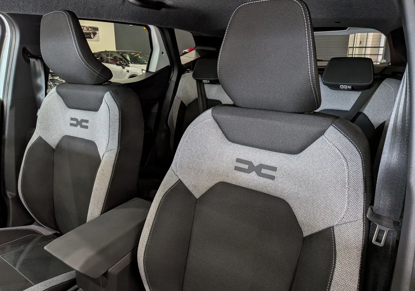 Vue rapprochée des sièges avant gris et noirs du Dacia Duster Hybrid-G 150 CH 4x4, avec logo distinctif brodé.