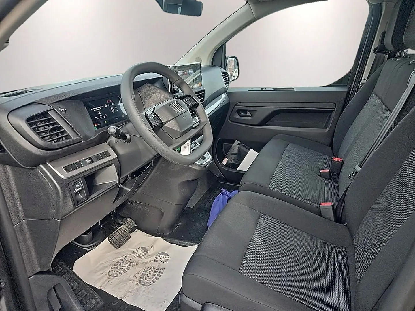 Vue intérieure côté conducteur du Fiat Scudo Combi 2026, sièges tissu bi-ton noir/gris et tableau de bord moderne.