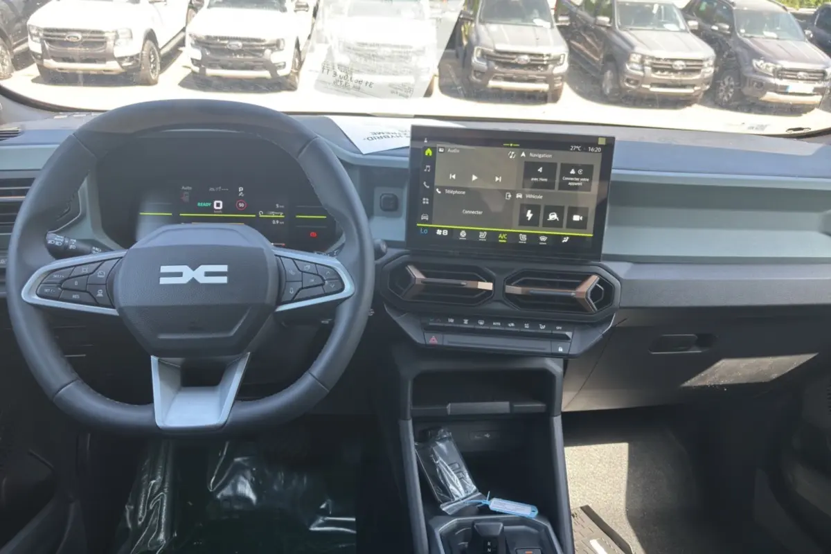 Vue intérieure frontale du tableau de bord du Dacia Duster Hybrid-G 150 avec écran tactile et volant cuir noir.