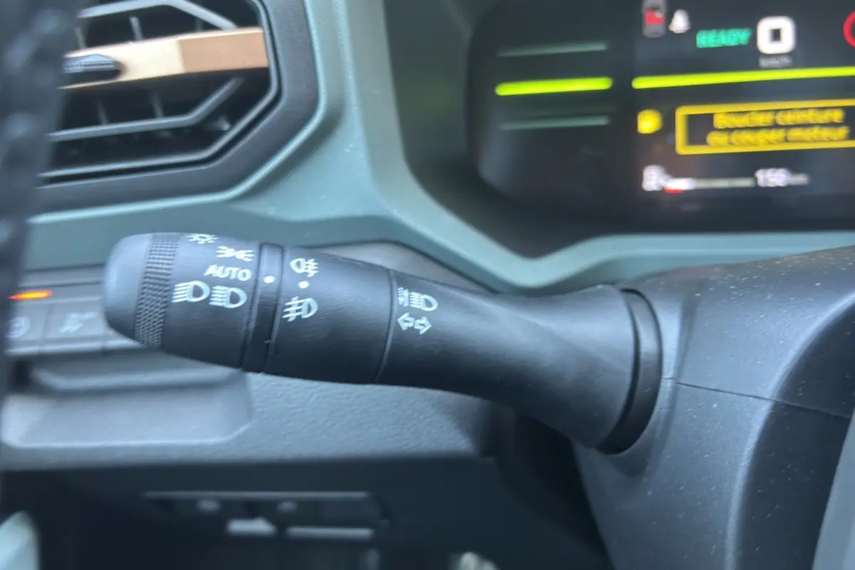 Gros plan sur la commande des feux à gauche du volant dans l'habitacle du Dacia Duster Hybrid-G 150 noir nacré 2026.