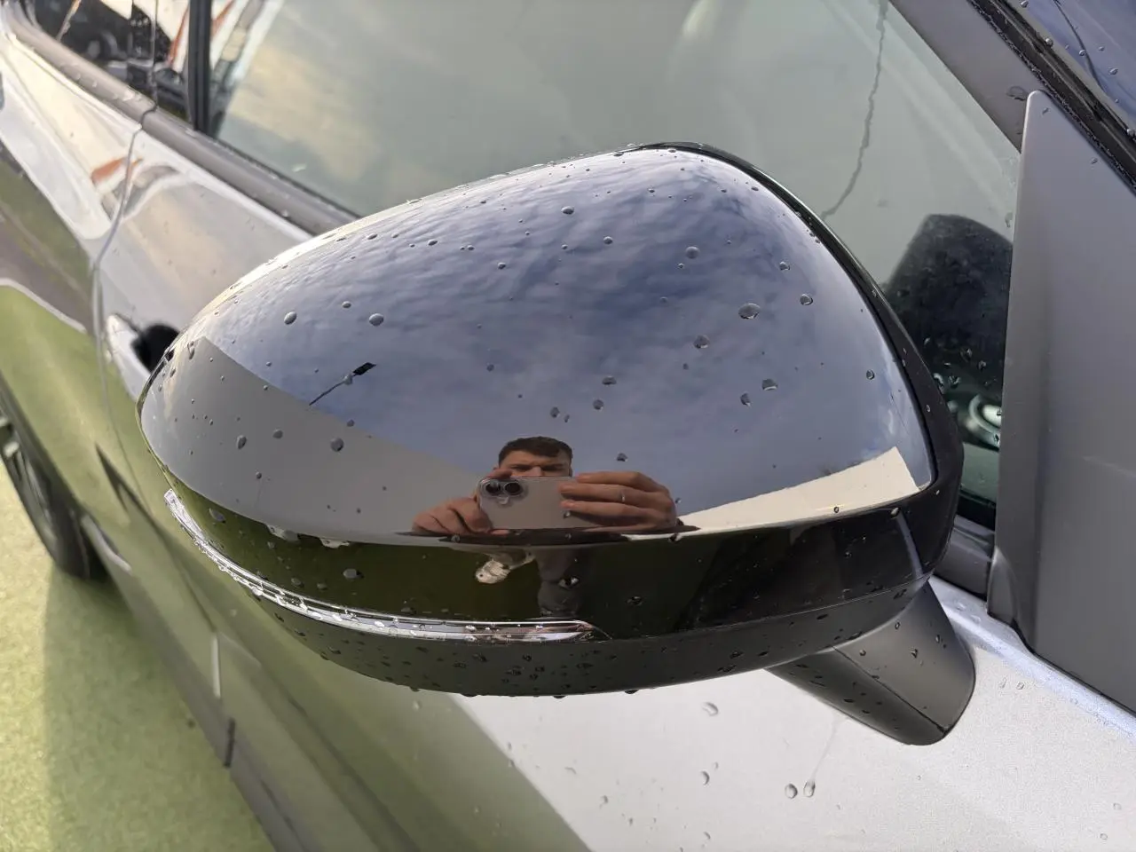 Rétroviseur noir métallisé côté gauche du Nissan Juke II 1.6 Hybrid 143 N-Connecta avec gouttes d'eau visibles.