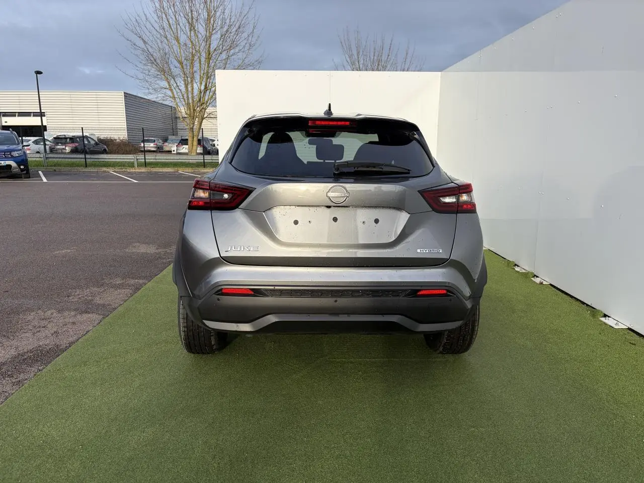 Vue arrière d'un Nissan Juke II hybride gris métallisé avec feux LED et antenne aileron de requin noire.