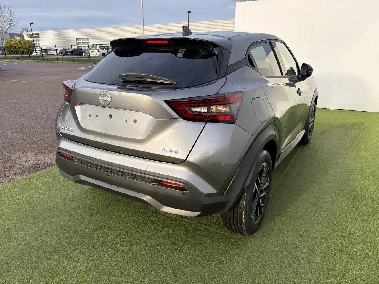 Vue 3/4 arrière droite d'un Nissan Juke II hybride gris métallisé avec feux LED et jantes alliage noires.