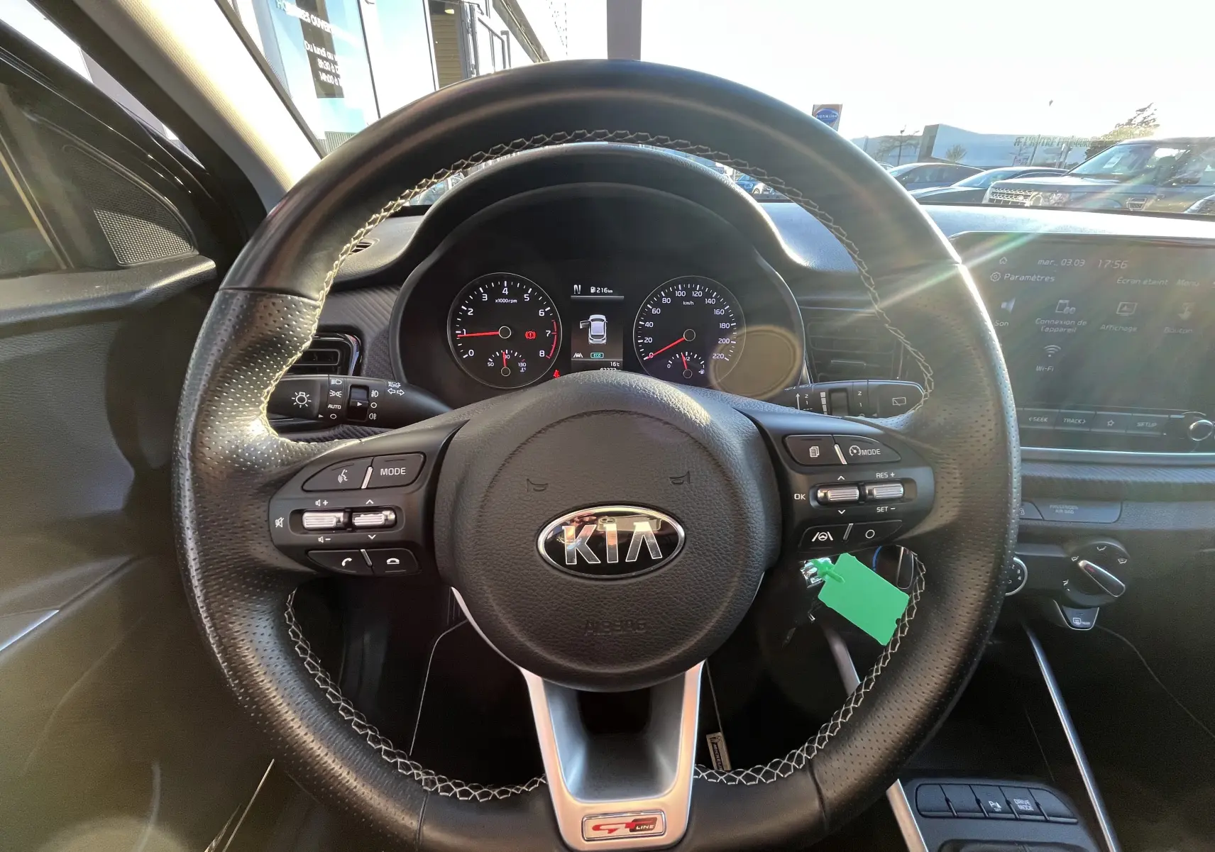 Vue intérieure centrée sur le volant noir perforé de la KIA Rio 1.0 GDI 100 Hybrid GT Line avec tableau de bord et écran tactile.