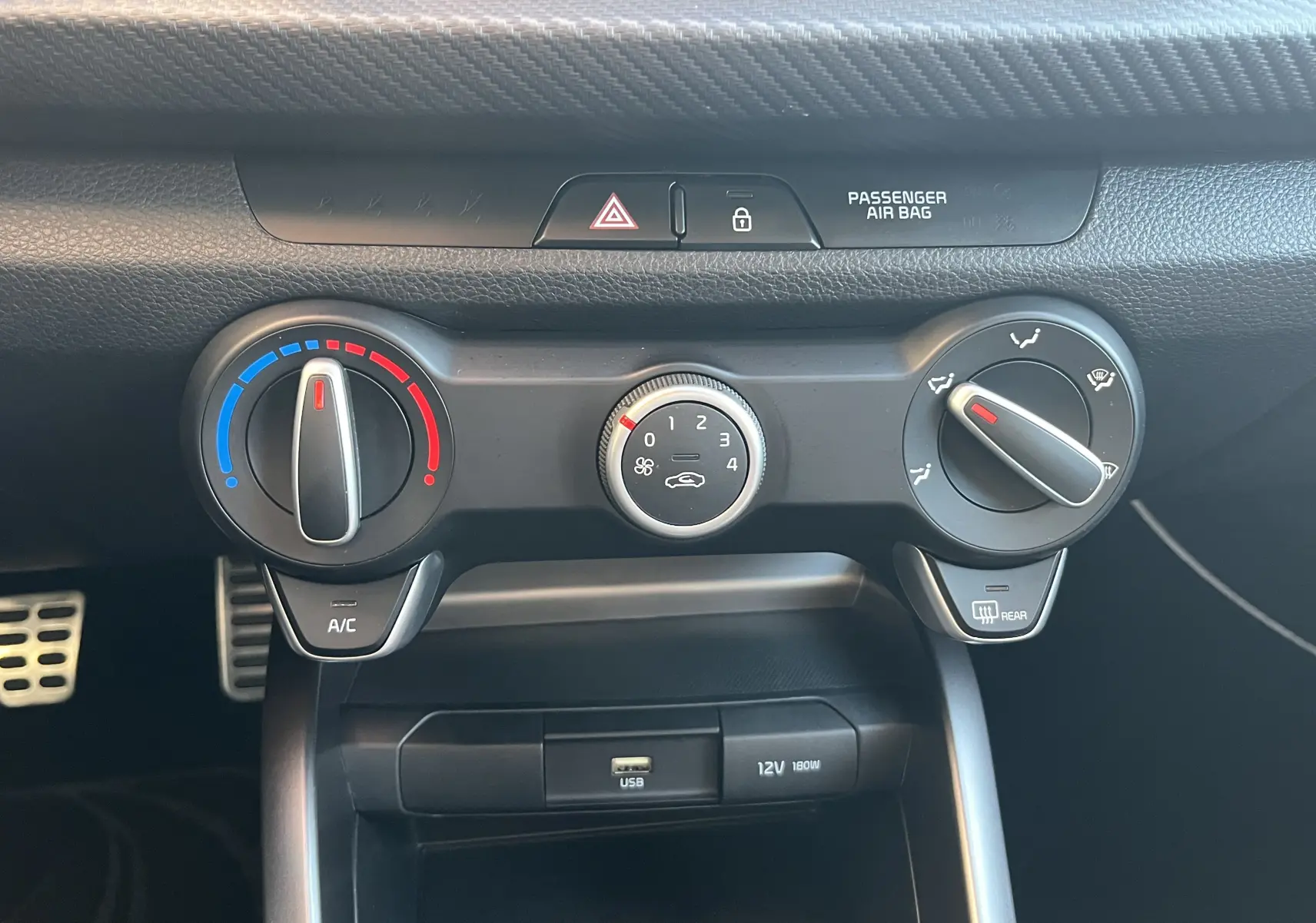 Vue rapprochée des commandes de climatisation et ventilation de la Kia Rio noire, avec réglages manuels et port USB visible.