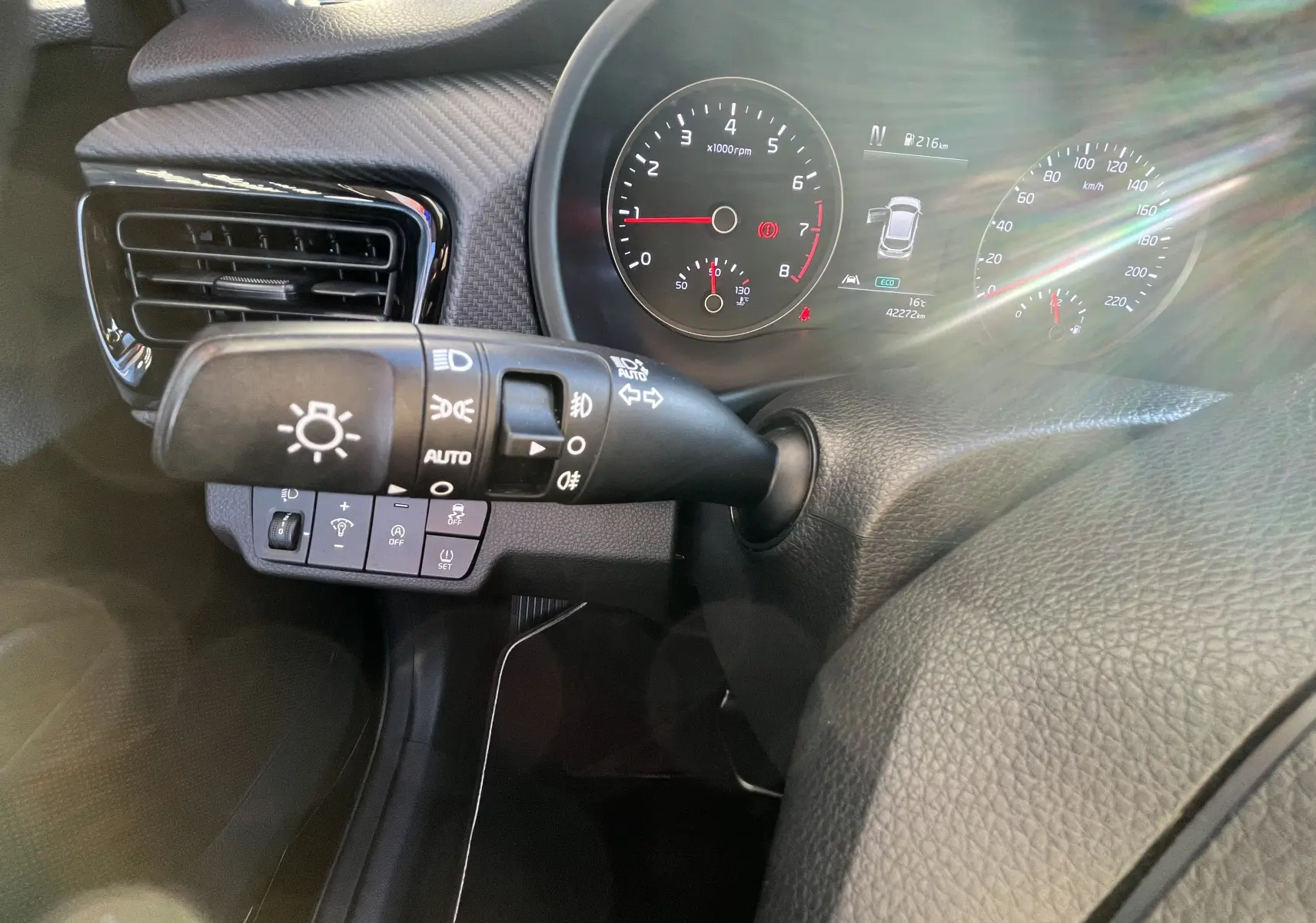 Gros plan sur la manette d’éclairage et le tableau de bord numérique d’une KIA RIO noire, version 2021, côté gauche du volant.