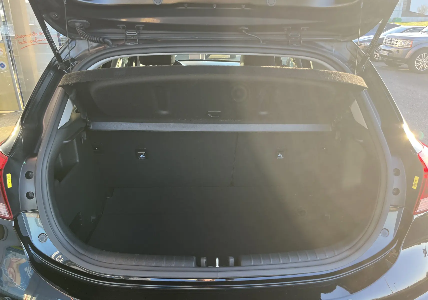 Coffre ouvert vu de l'arrière d'une KIA RIO noire 2021, montrant l'espace de chargement vide et la tablette arrière relevée.