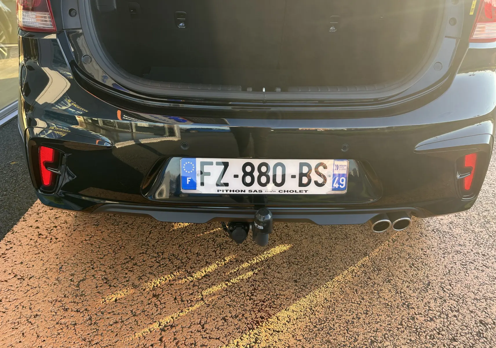 Vue arrière rapprochée de la Kia Rio noire 2021 avec coffre ouvert, double sortie d’échappement et attelage visible.