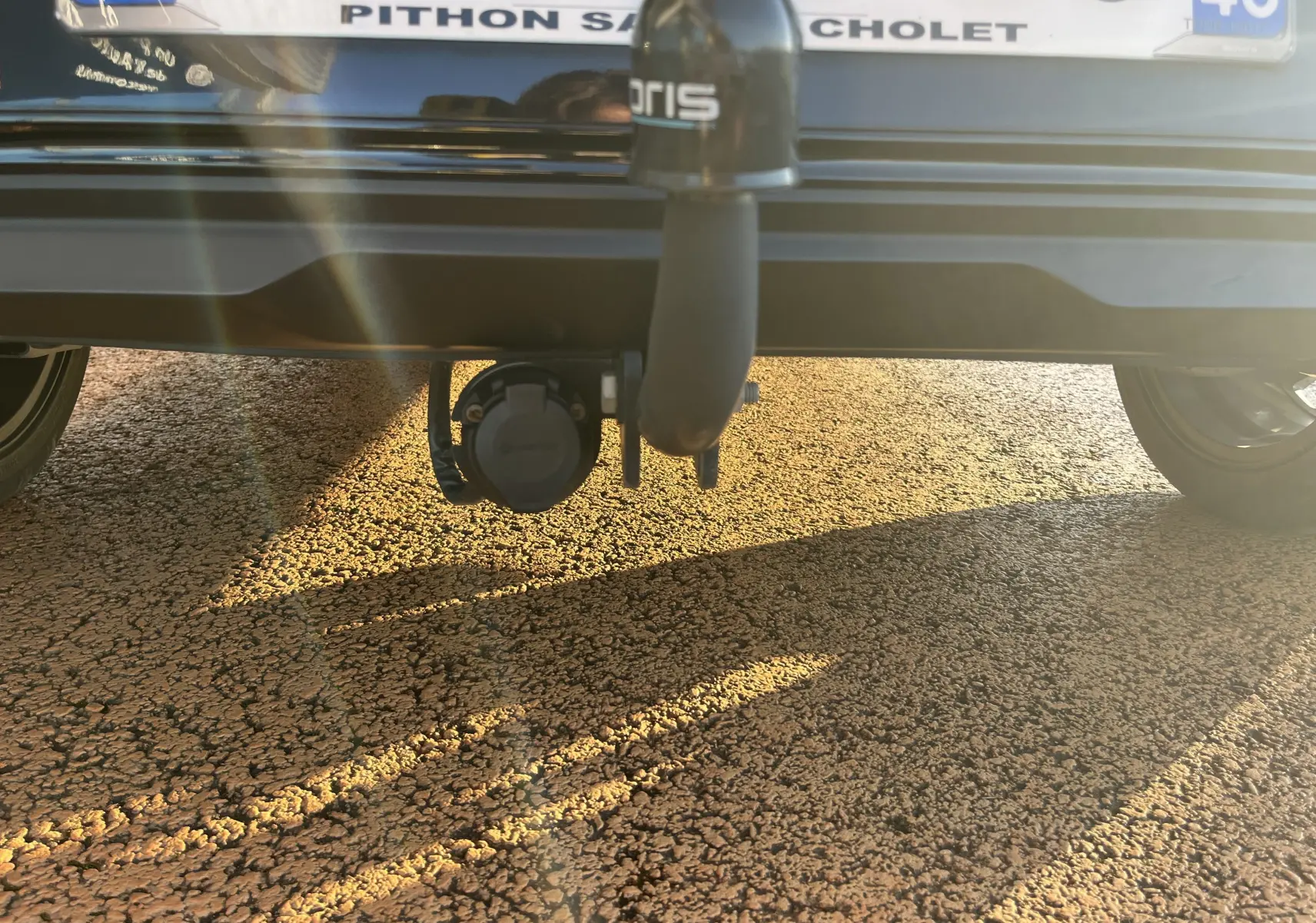 Vue rapprochée de l'attelage noir sous le pare-chocs arrière d'une KIA Rio 2021, avec prise électrique visible.