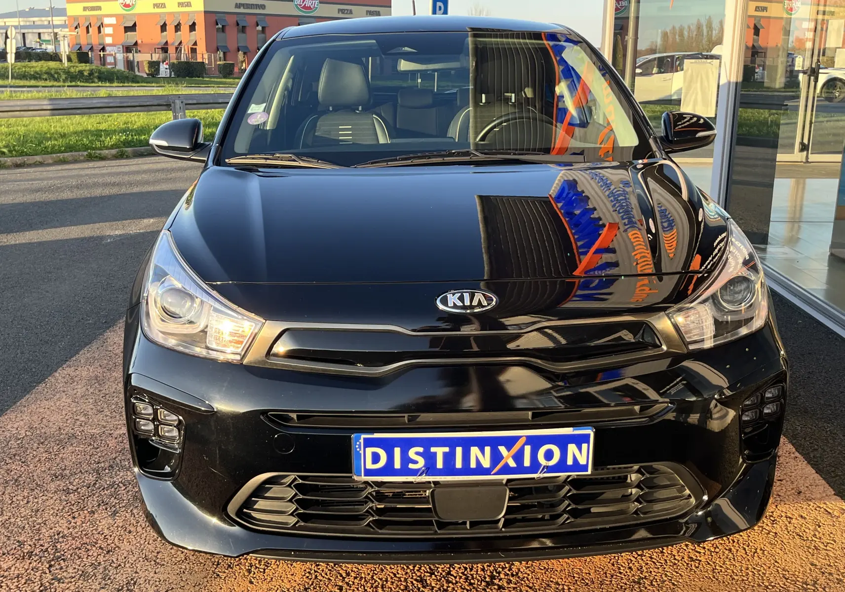 Vue avant d'une KIA Rio 1.0 GDI 100 Hybrid GT Line noire, avec calandre distinctive et phares LED allumés.