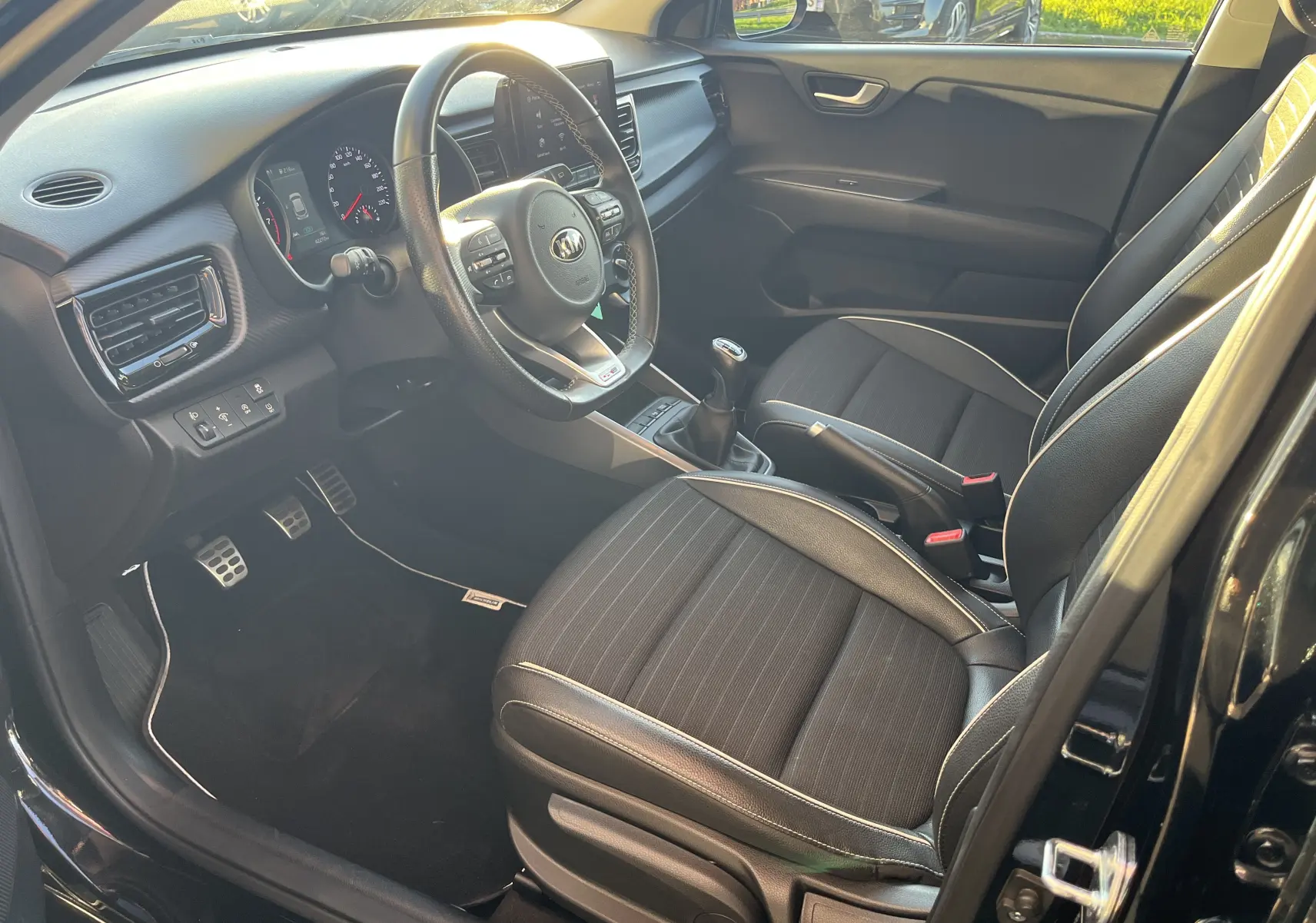 Intérieur noir de la KIA RIO 1.0 GDI Hybrid 2021, vue côté conducteur avec volant multifonction et sièges tissu-cuir.