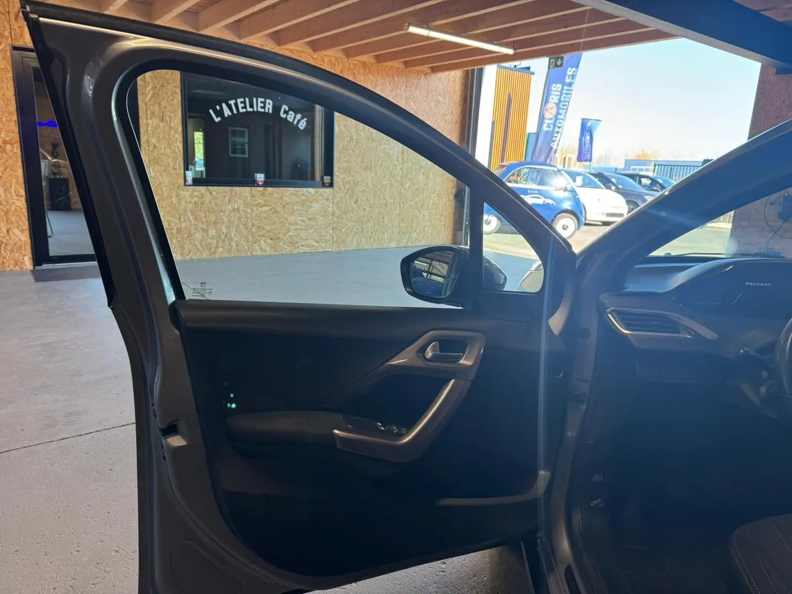 Vue intérieure côté gauche de la porte avant ouverte d’un Peugeot 2008 gris, montrant la garniture et la poignée.