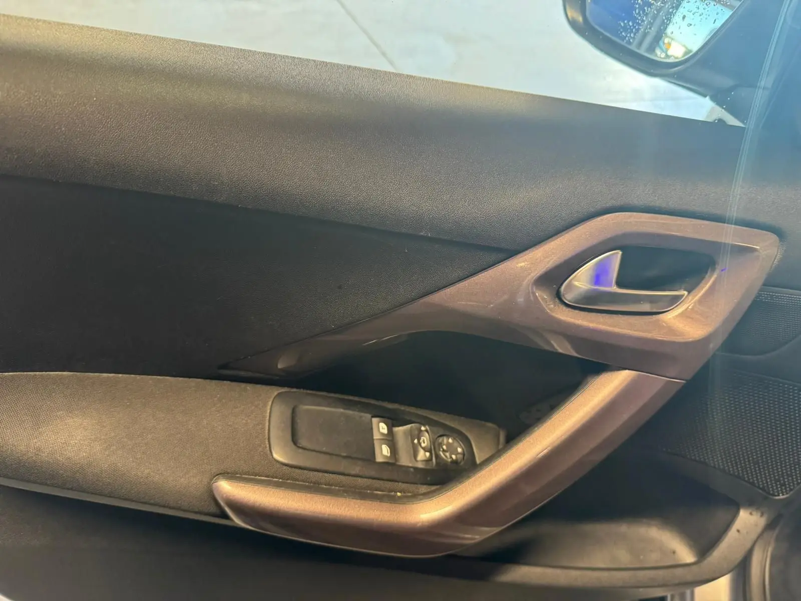 Détail de la porte intérieure côté conducteur du Peugeot 2008 gris, avec commandes des vitres et poignée intégrée.