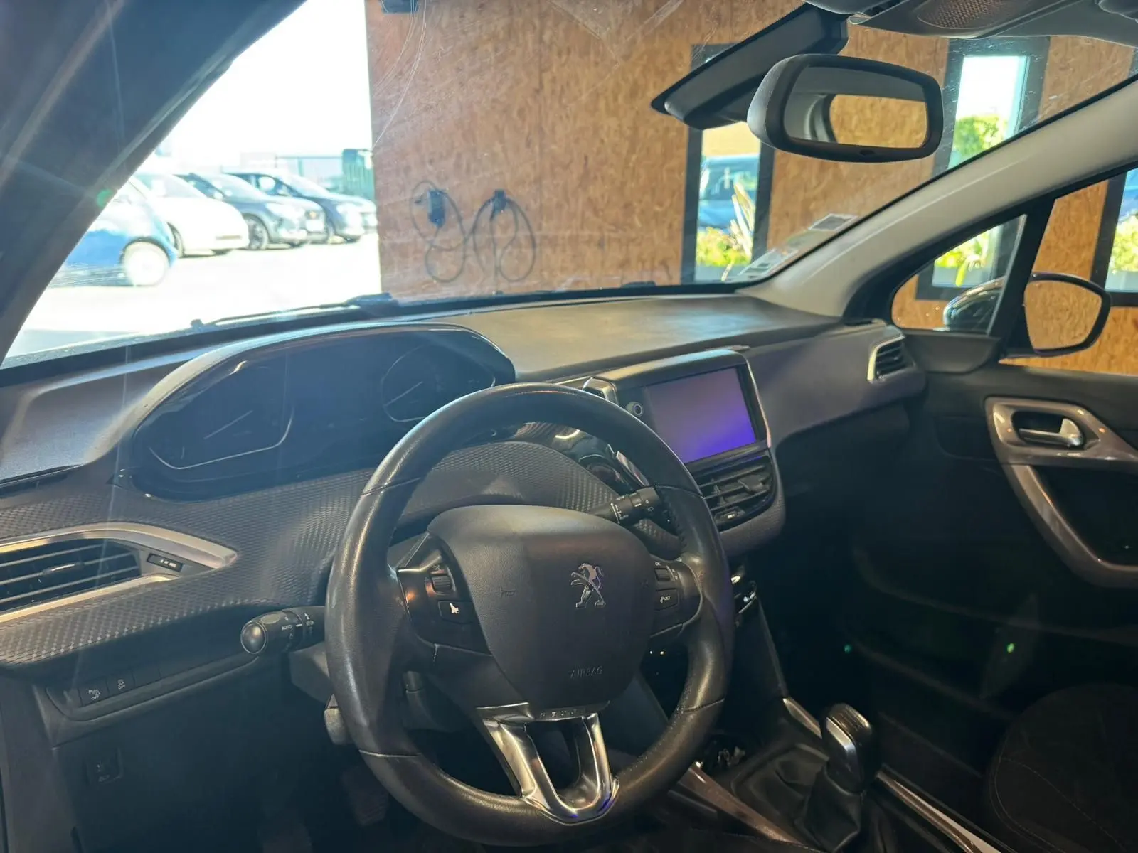 Vue intérieure côté conducteur du Peugeot 2008 gris, montrant le volant, tableau de bord et écran tactile central.