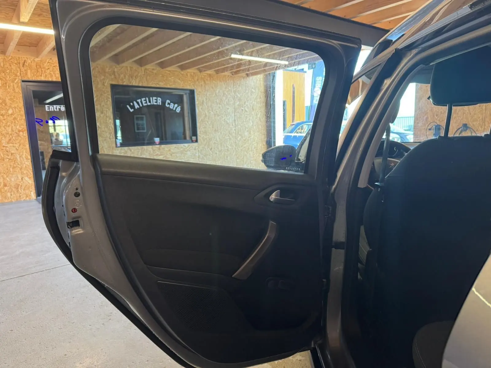 Vue intérieure côté gauche de la porte arrière ouverte d’un Peugeot 2008 gris, montrant la garniture noire et la poignée.