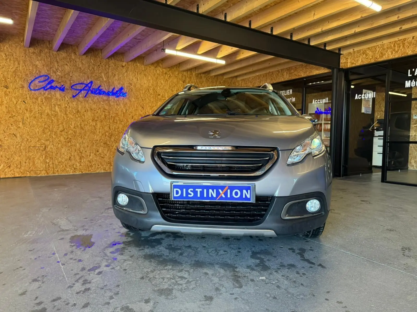 Vue frontale d'un Peugeot 2008 gris 2016 avec calandre noire et plaque d'immatriculation Distinxion dans un showroom.