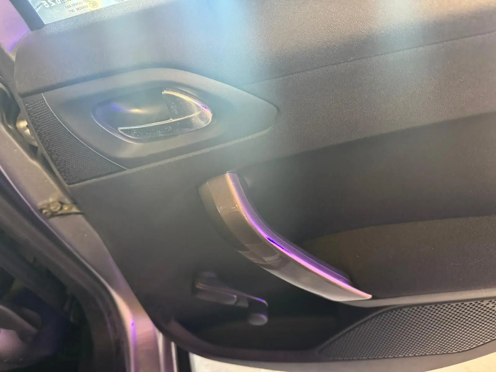 Vue rapprochée de la poignée intérieure côté gauche d’une Peugeot 2008 gris, avec manivelle de vitre manuelle visible.