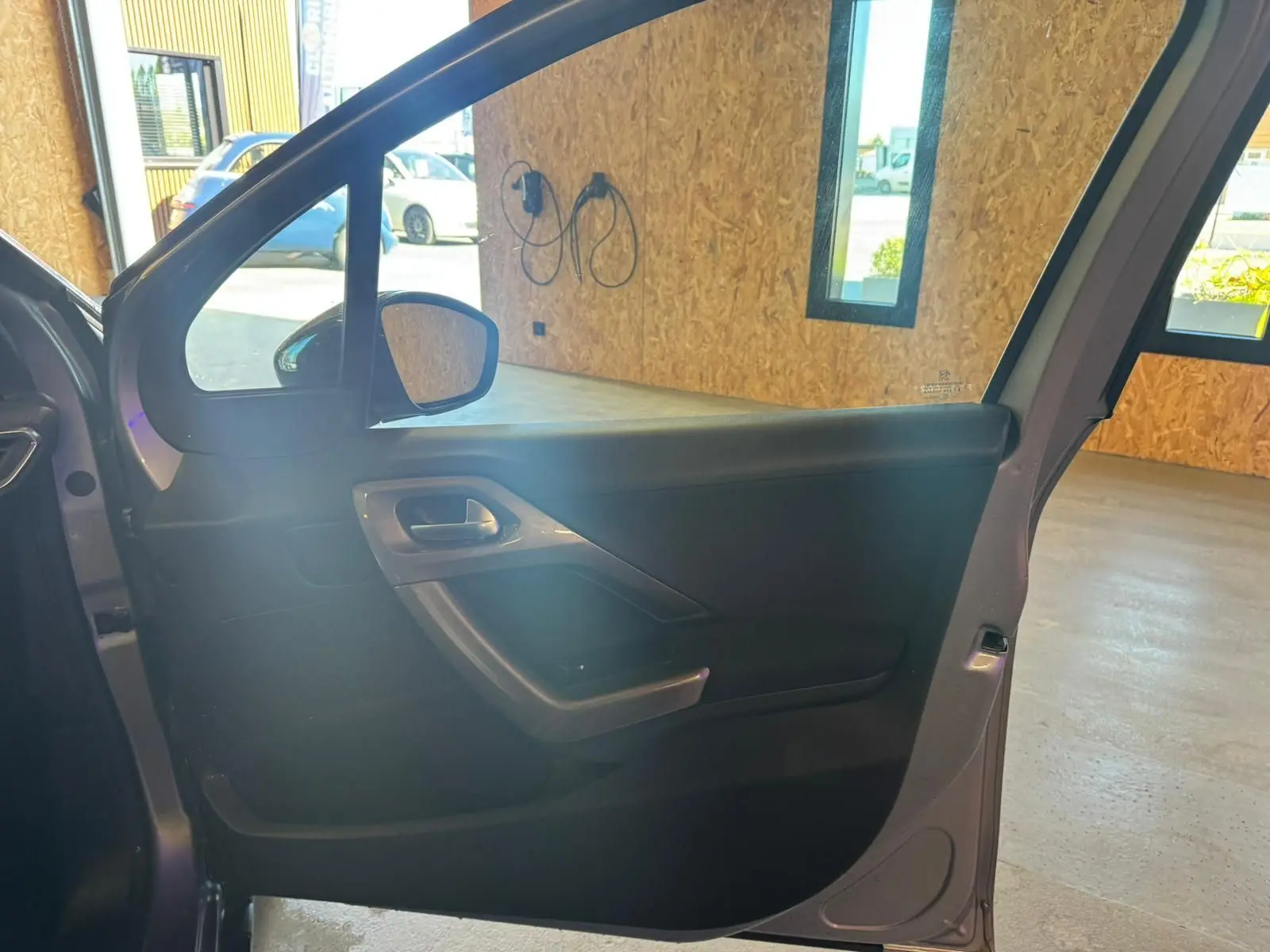 Vue intérieure de la porte avant gauche ouverte d’un Peugeot 2008 gris, mettant en valeur la poignée et les commandes.