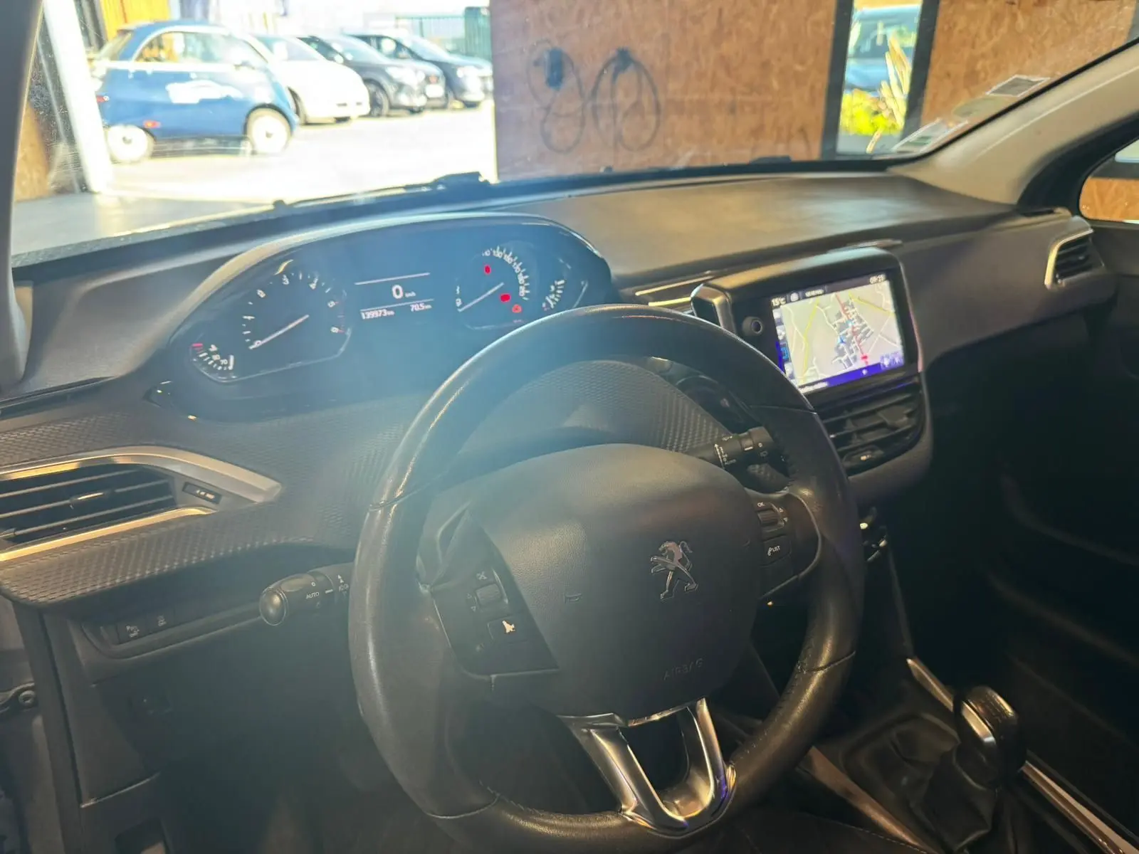 Vue intérieure du poste de conduite du Peugeot 2008 gris, avec volant, tableau de bord digital et écran GPS central.