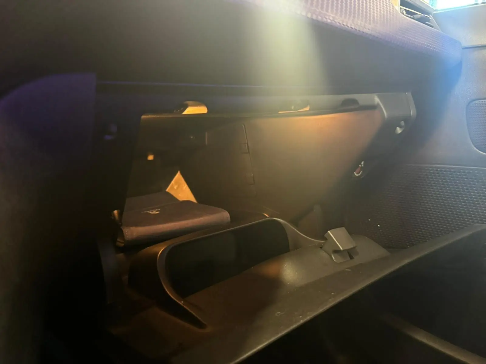 Intérieur du Peugeot 2008 1.6 HDI 100 STYLE 2016 montrant la boîte à gants ouverte avec un livret à l'intérieur, ambiance sombre.