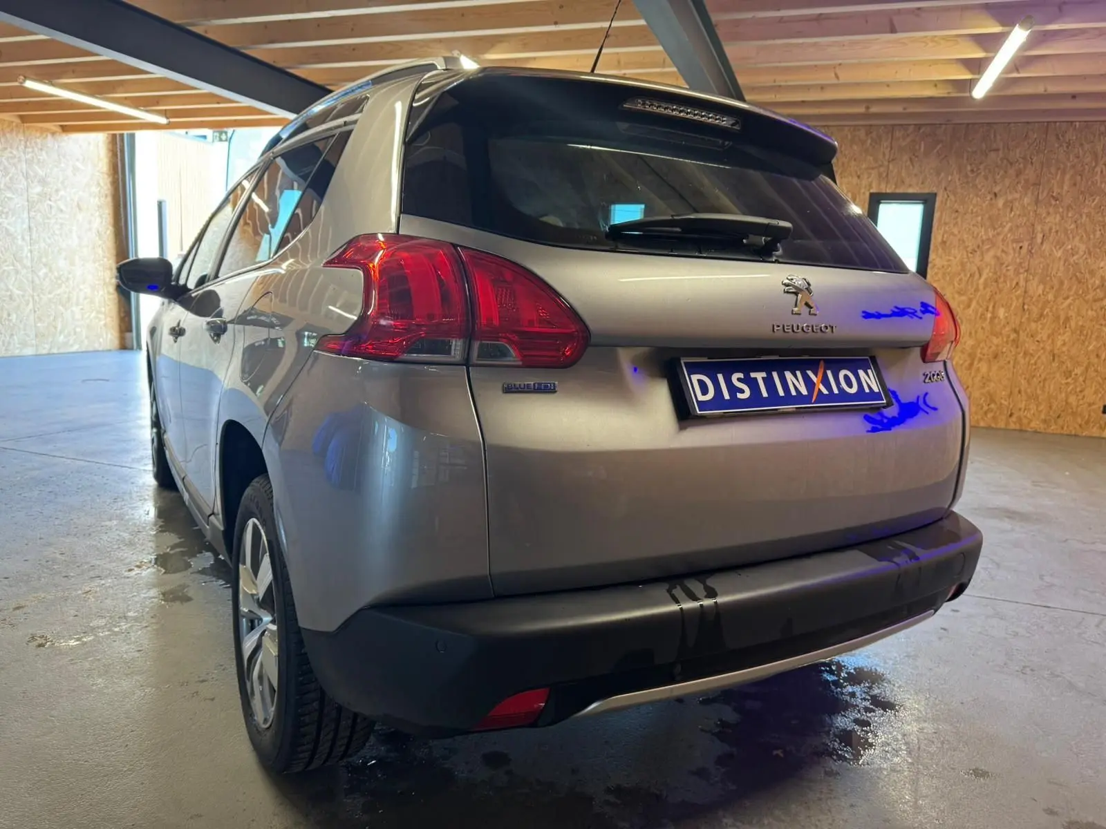 Vue 3/4 arrière droite d'un Peugeot 2008 gris 2016 avec feux arrière rouges et logo distinctif dans un garage.