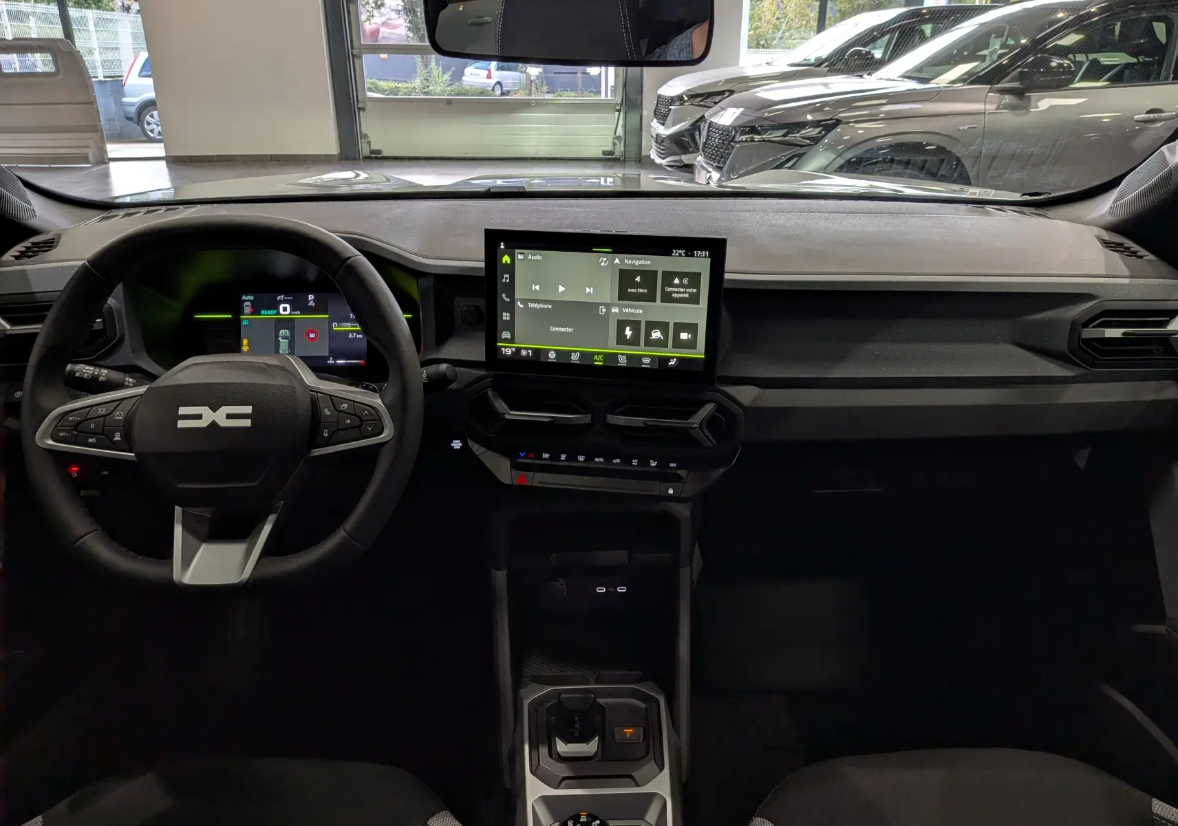 Vue intérieure frontale du tableau de bord du Dacia Duster Hybrid-G blanc, avec écran tactile central et volant multifonction.