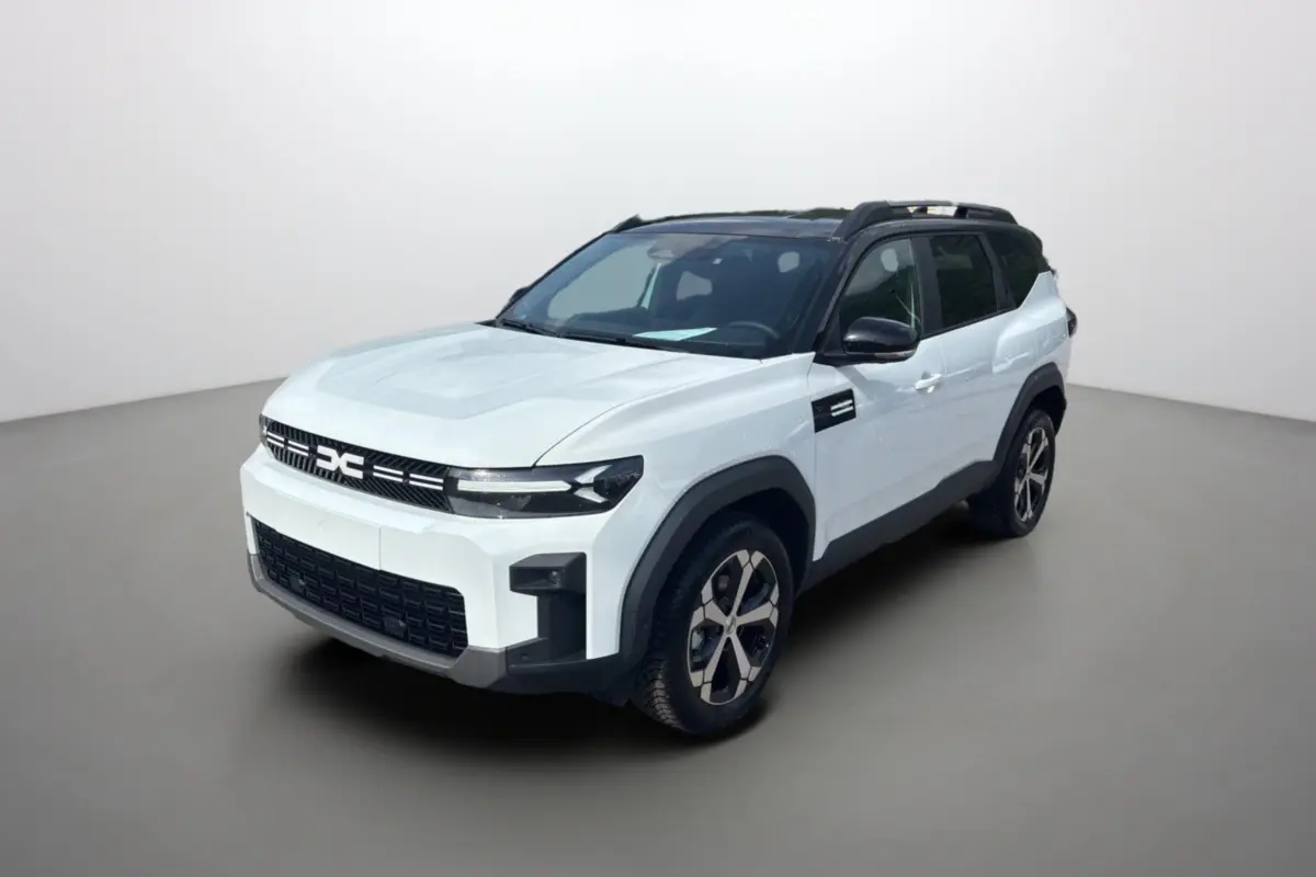 Vue 3/4 avant droit du Dacia Bigster blanc toit noir avec jantes alu et barres de toit noires.