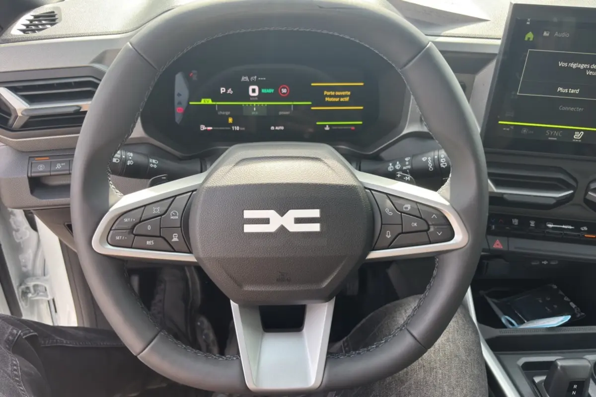 Vue centrée sur le volant cuir du Dacia Bigster Hybrid 150, avec tableau de bord digital et écran tactile visible.