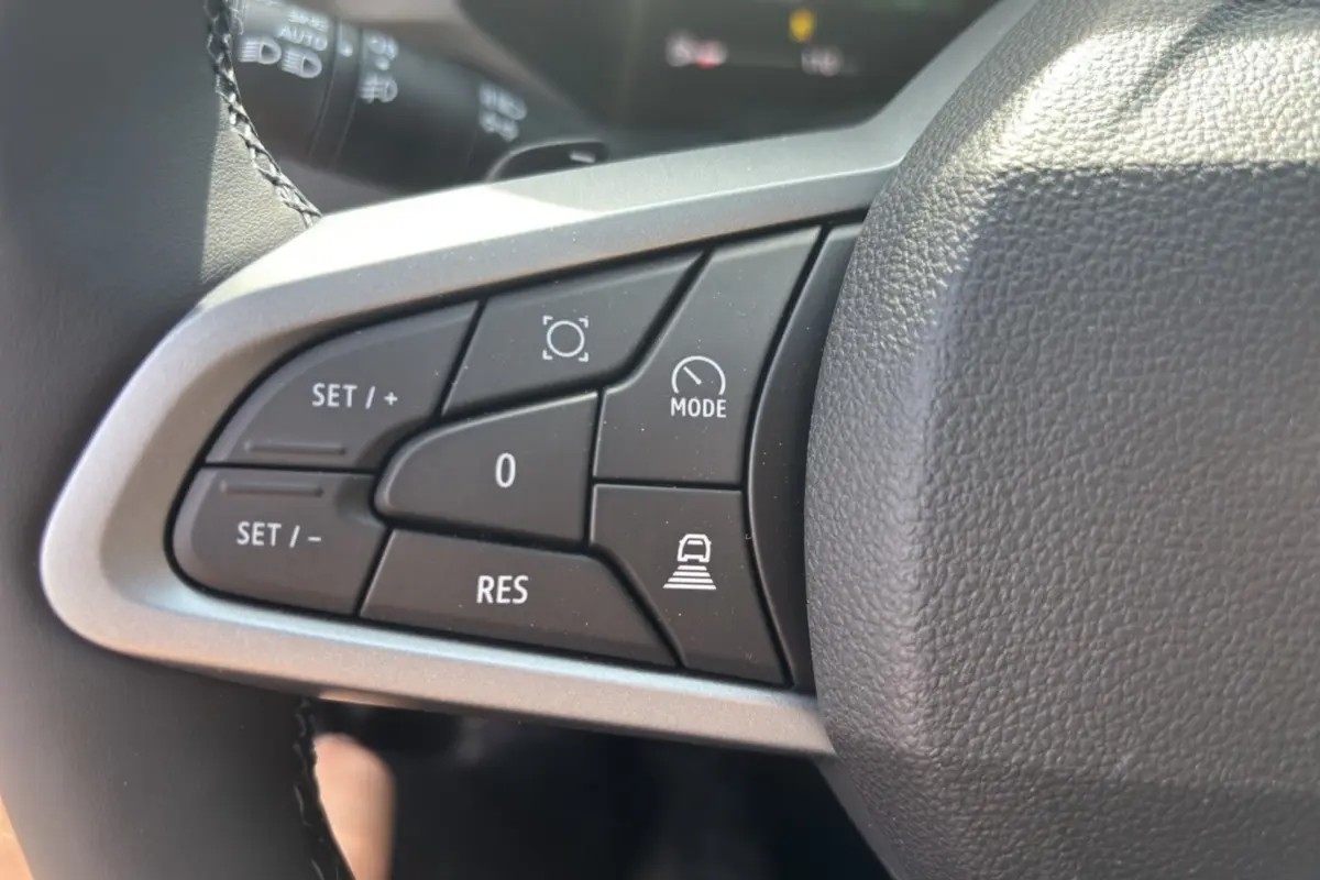 Gros plan sur les commandes au volant cuir du DACIA BIGSTER Hybrid 150, boutons de régulateur et mode conduite visibles.