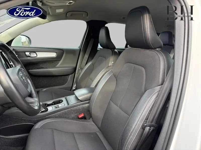 Vue intérieure côté conducteur du Volvo XC40 blanc, mettant en valeur les sièges en tissu noir et la console centrale.