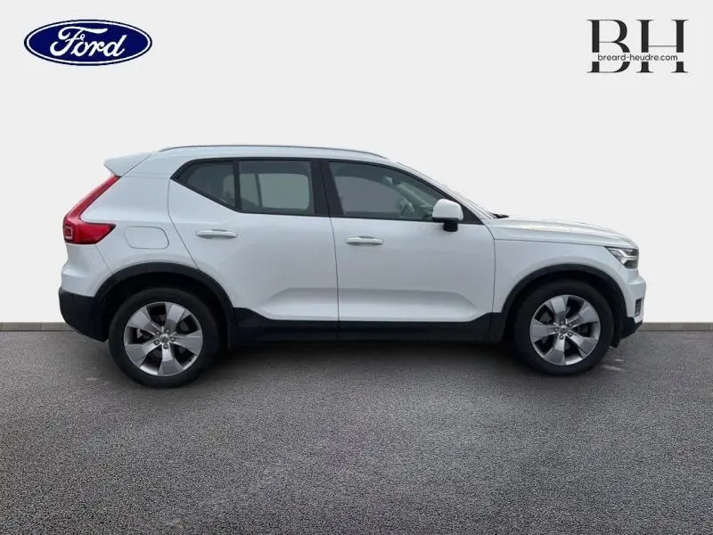 Profil côté droit d'un Volvo XC40 blanc glace de 2018 avec jantes alliage et barres de toit visibles.