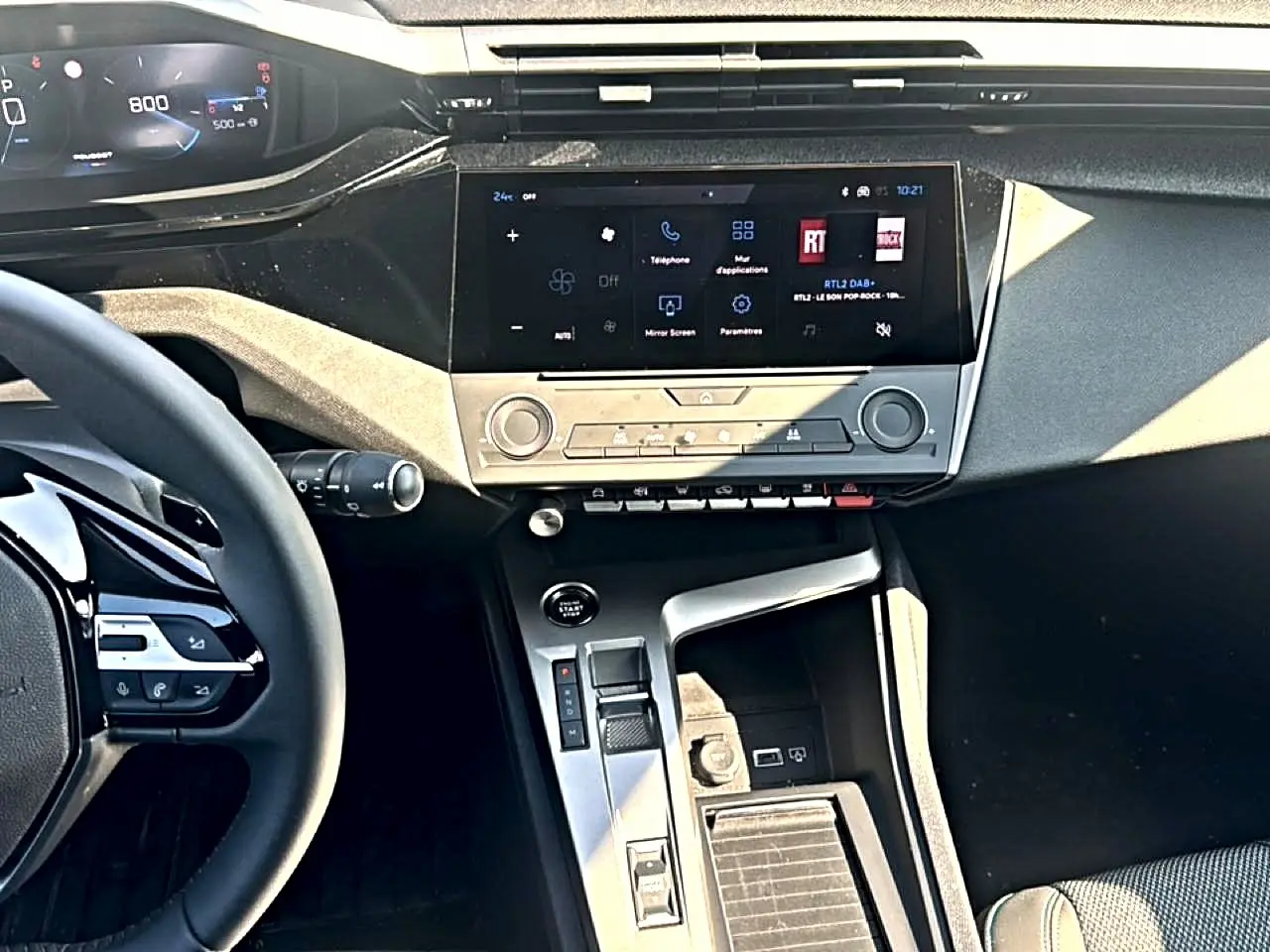 Vue intérieure centrée sur la console centrale et l'écran tactile de la Peugeot 308 2025, volant multifonction visible à gauche.